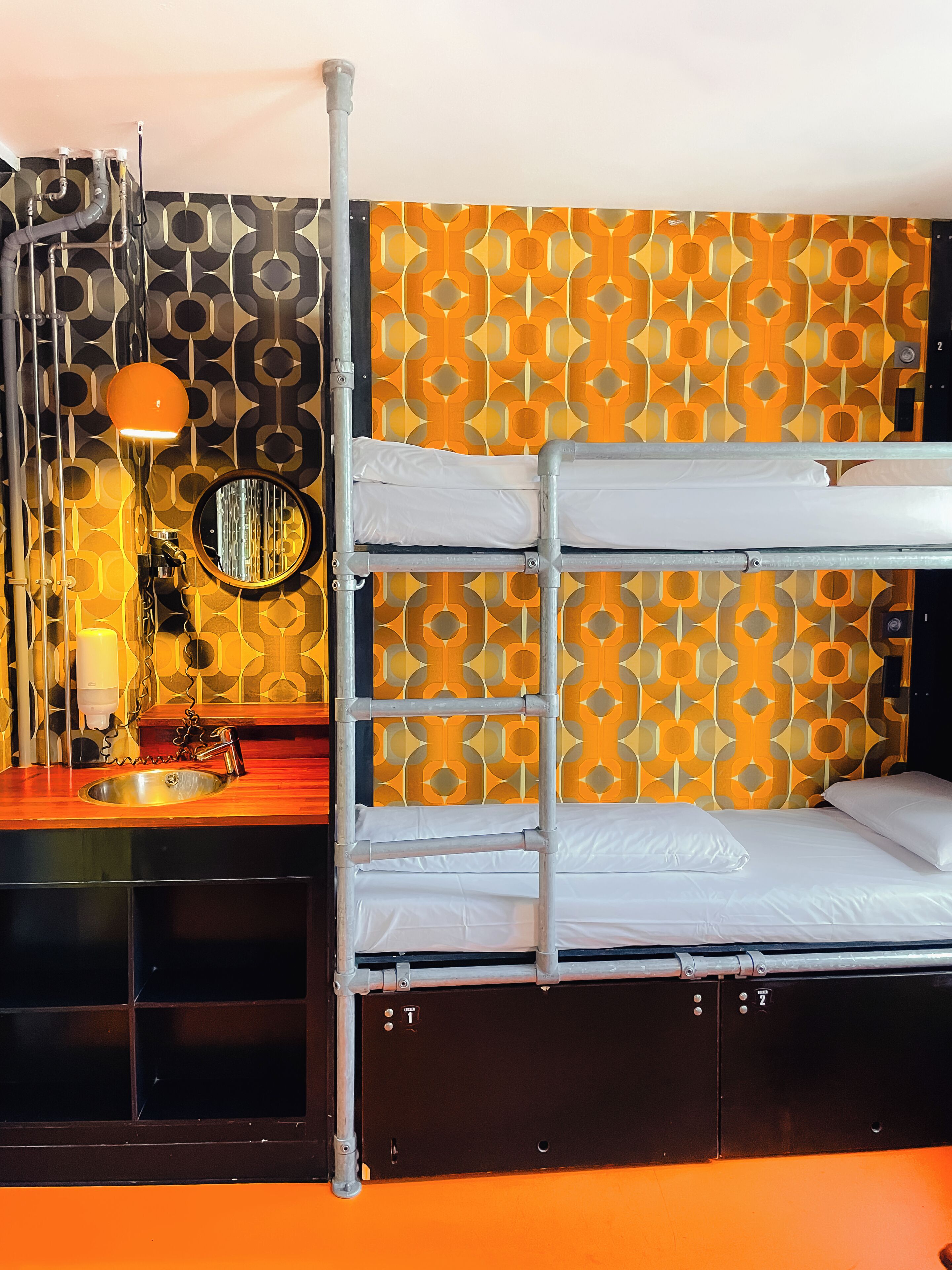 Ein Stockbett mit Metallgestell, ein Waschbecken, ein Spiegel und eine Wand mit Muster.