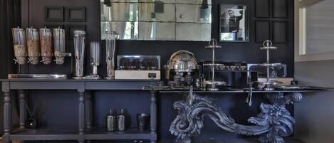 A bar area with a dark wood table, glass dispensers, a coffee machine, and a decorative metal stand.