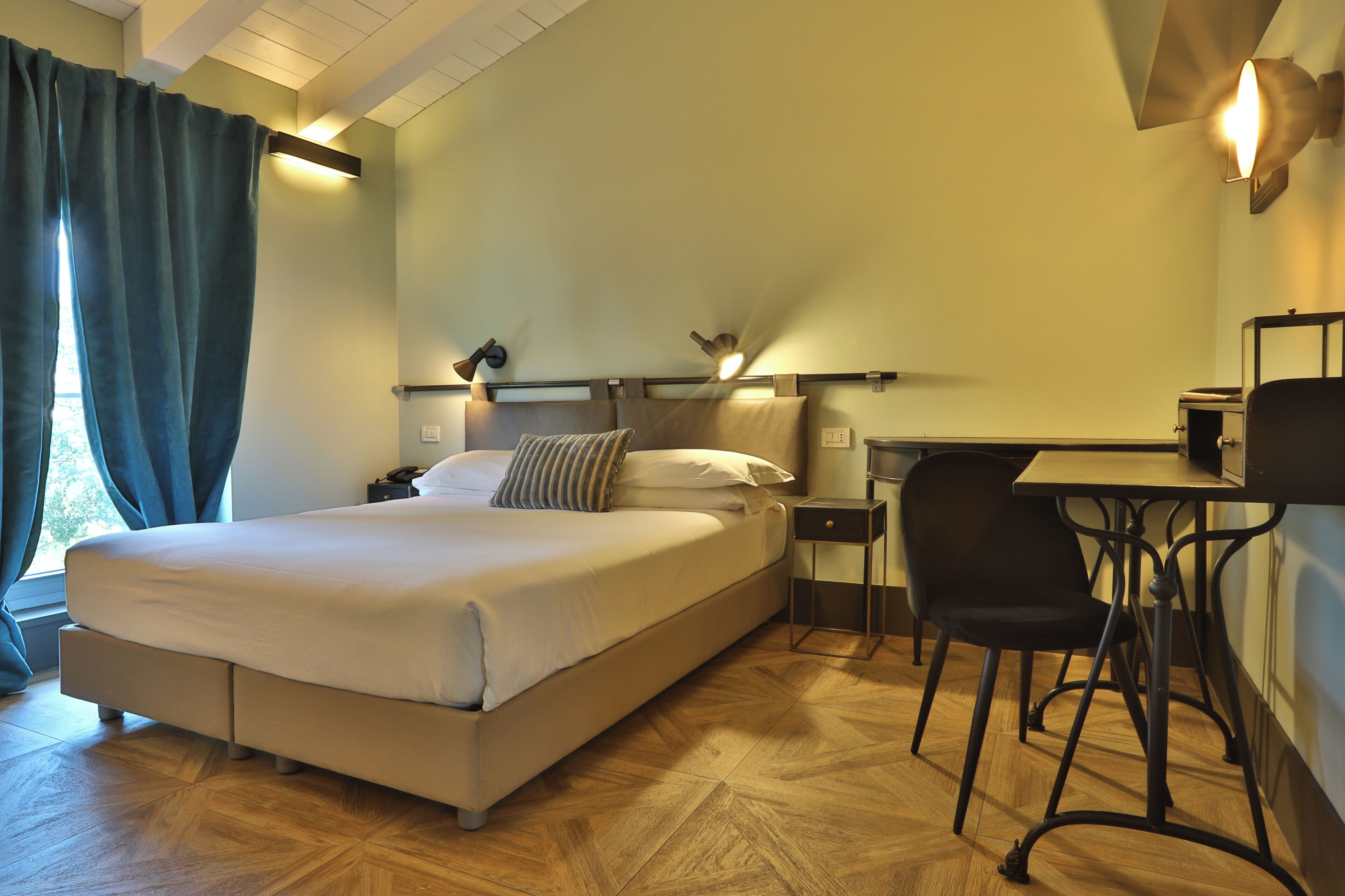 A bedroom with a bed, bedside table, lamp, chair, and a desk with a chair.