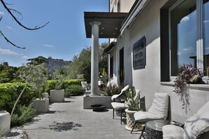 A patio area with outdoor seating, a fire pit, and a view of a building with a sign. - Hotel Le Corderie (Trieste)