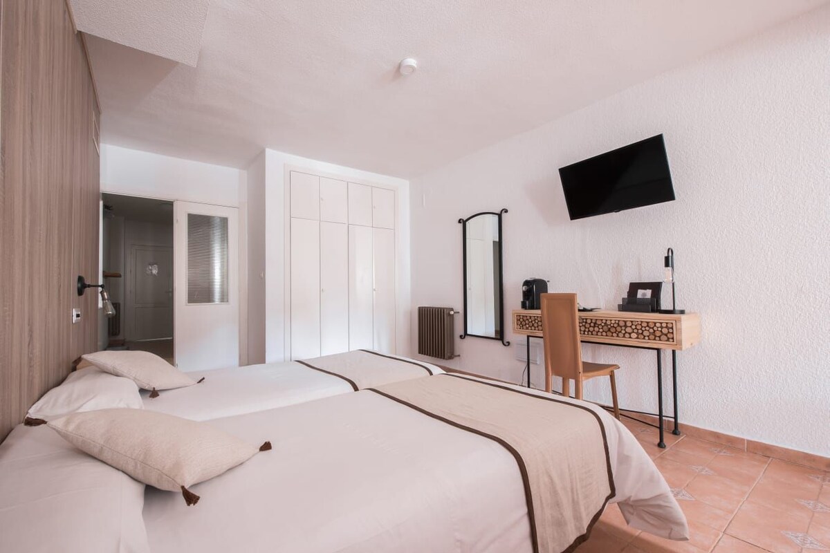 A hotel room with two beds, a desk, a chair, a television, and a mirror.