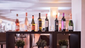 Une rangée de bouteilles de vin sur une étagère, avec des plantes en pot en dessous.