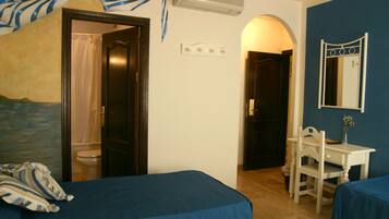 Una habitación con dos camas, un escritorio, una silla, un espejo y la puerta del baño.