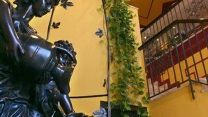 Une statue représentant une femme tenant un enfant, un escalier avec une rampe et un mur orné d’un motif géométrique.