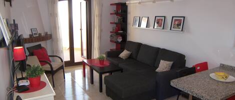 A living room with a sofa, a dining table, a chair, a small table with a plant, and a TV.