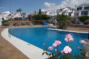 Relax by the serene pool surrounded by Mediterranean-style buildings and lush greenery.