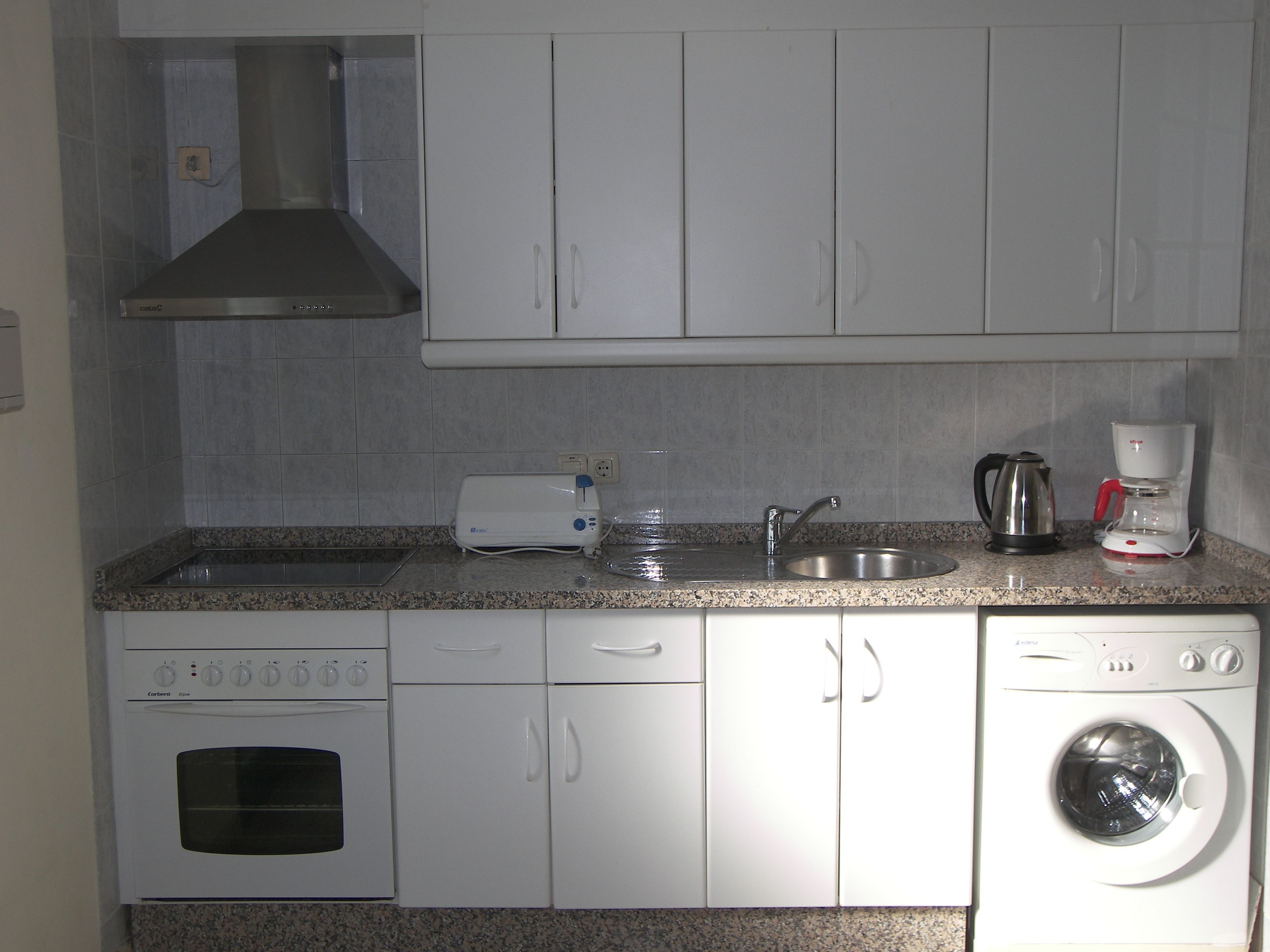Een functionele keuken met een inbouwoven, een wasmachine, een koffiezetapparaat en een broodrooster.