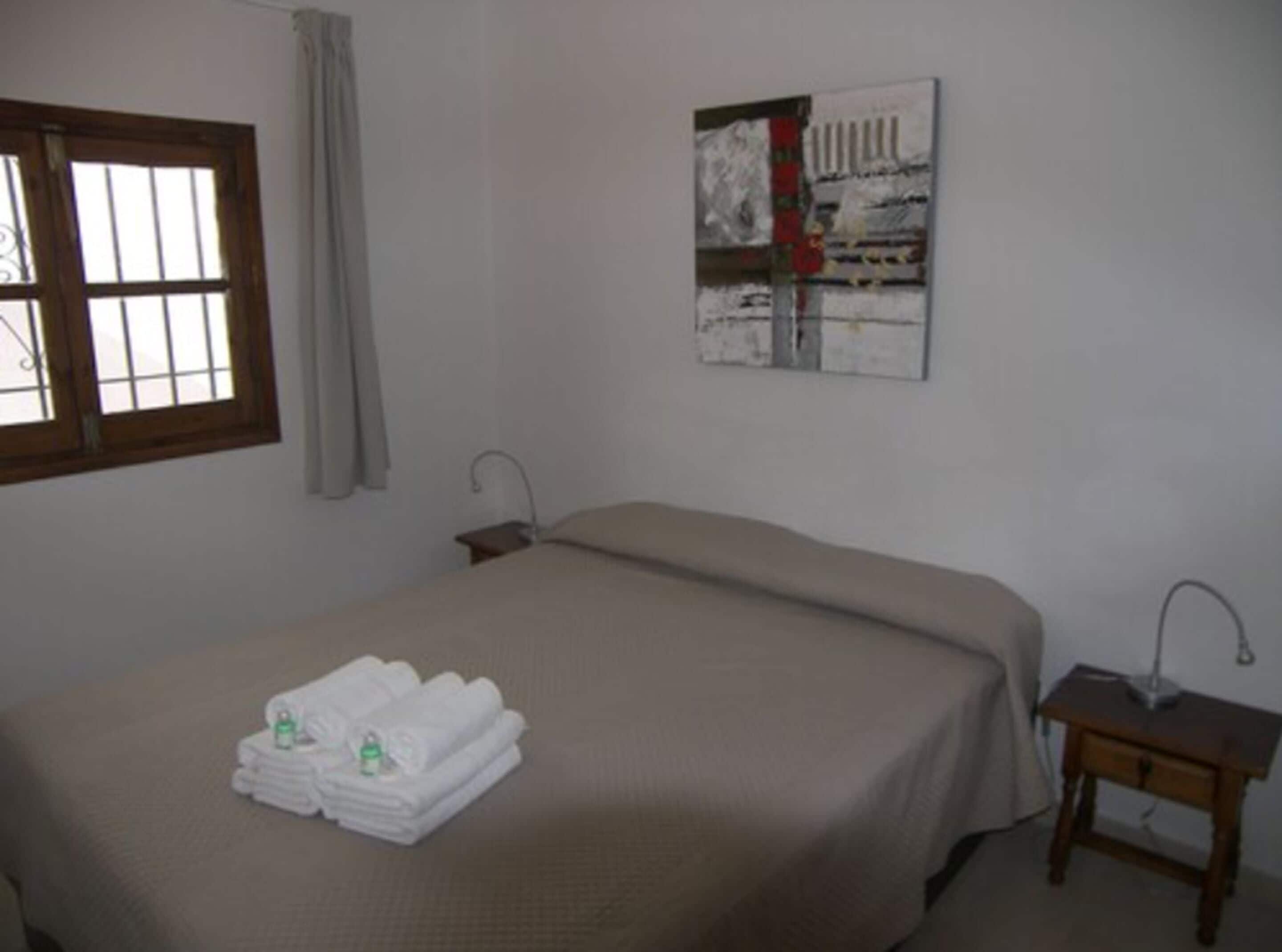 A bedroom with a bed, a nightstand, a window, and a painting on the wall.