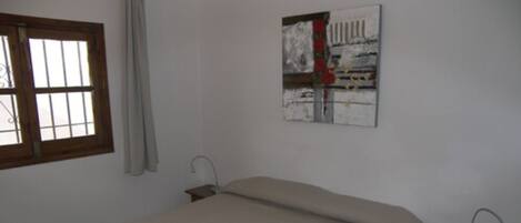 A bedroom with a bed, a nightstand, a window, and a painting on the wall.