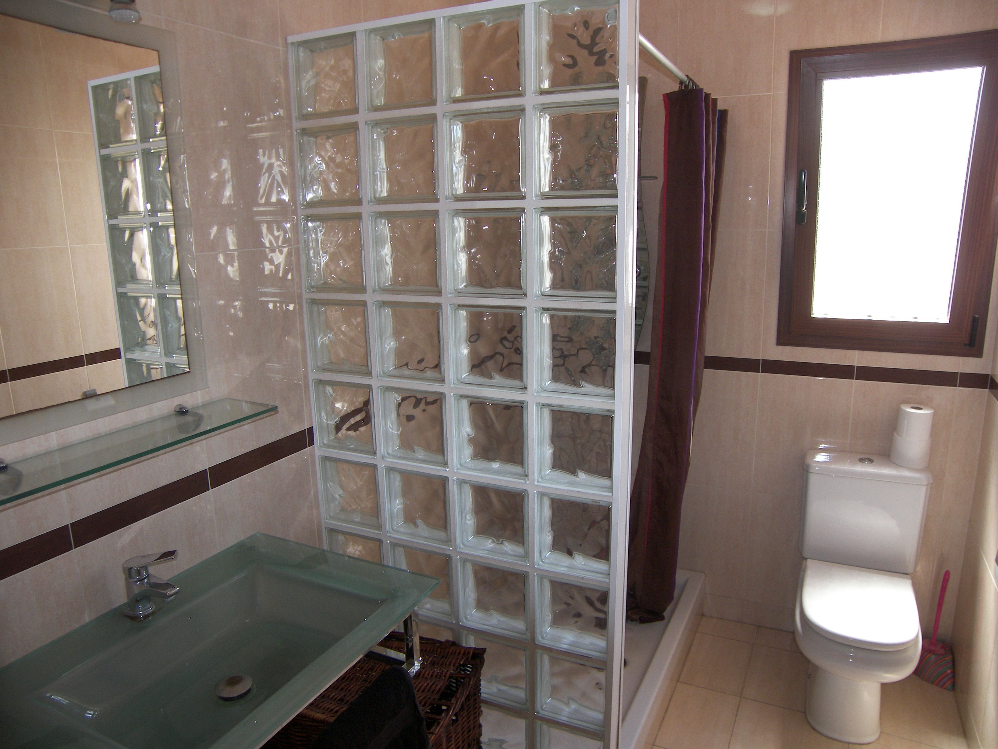 Un bany amb una dutxa de vidre, un lavabo de vidre i un vàter.