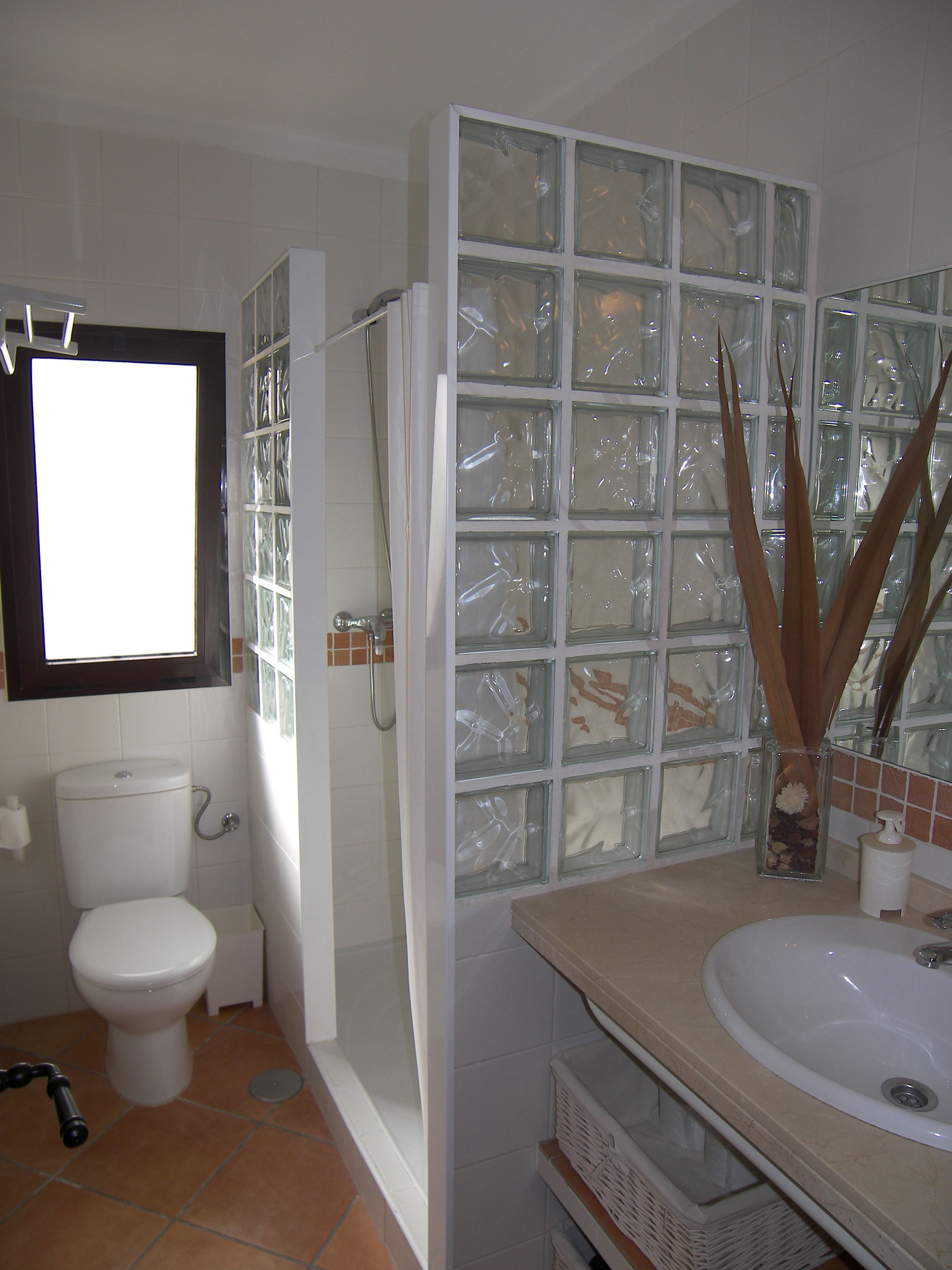 A bathroom with a glass shower enclosure, a toilet, and a sink with a mirror above it.