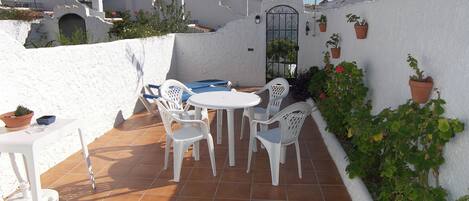 Een terras met witte kunststof stoelen en een tafel, omringd door witte muren en potplanten.