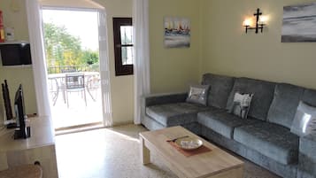 Una sala de estar con un sofá gris, una mesa de centro de madera, un televisor y un comedor con una mesa y sillas.