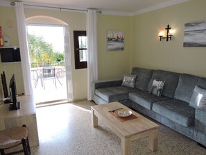 Relax in this inviting living room with a sofa, coffee table, and wicker chair, featuring a TV and artwork above.