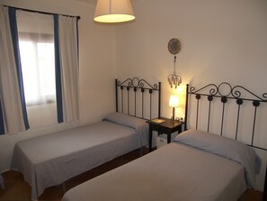 Two single beds with striped bedspreads are positioned against a wall, accompanied by a bedside table and a single lamp.