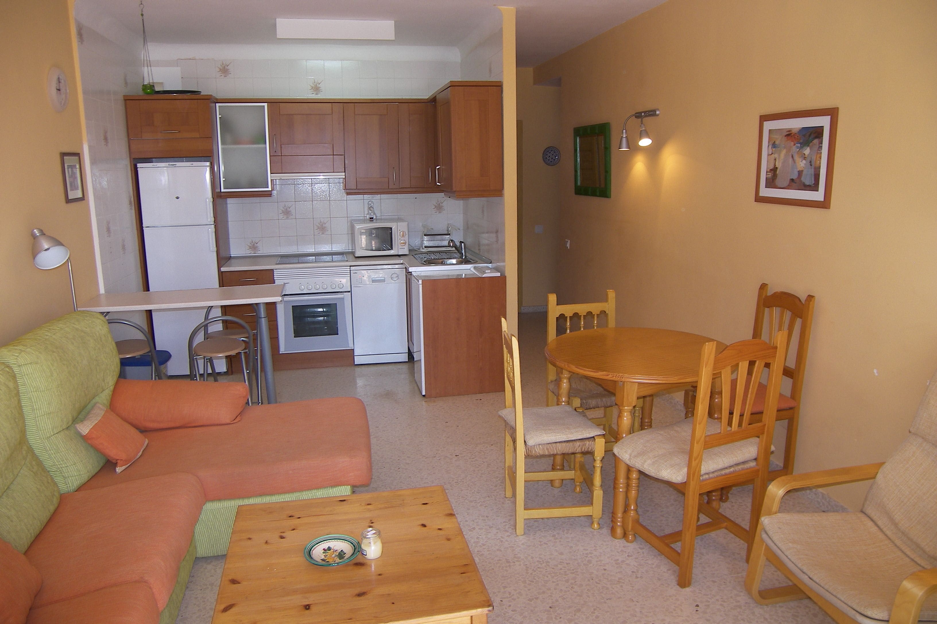 Een compact leefruimte met een kitchenette, een eettafel met stoelen en een bank.
