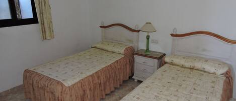 A room with two single beds, a nightstand with a lamp, and two framed pictures on the wall.