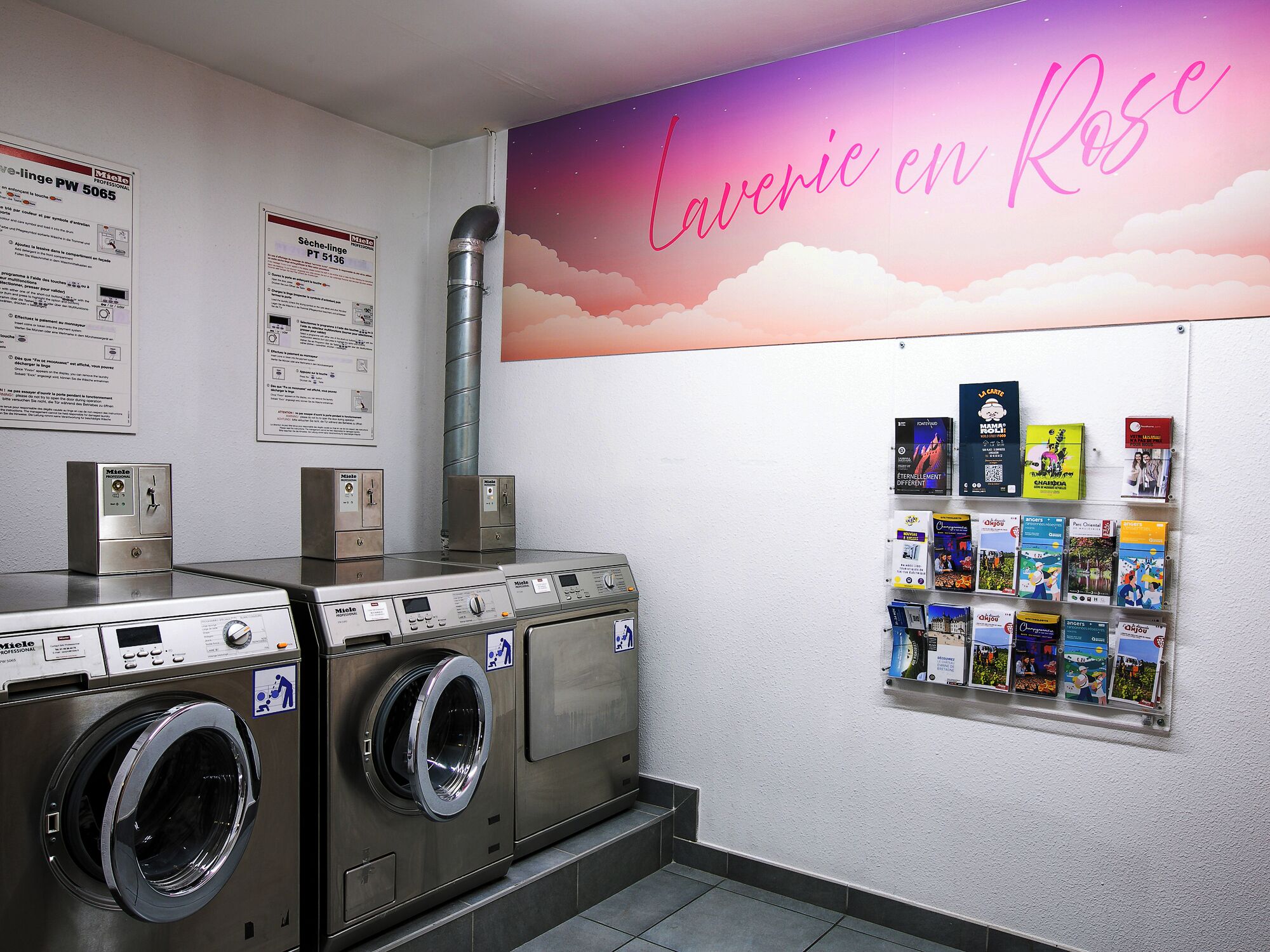A laundry area with industrial washers and dryers, informational posters on the wall, and a bulletin board with various items pinned to it.
