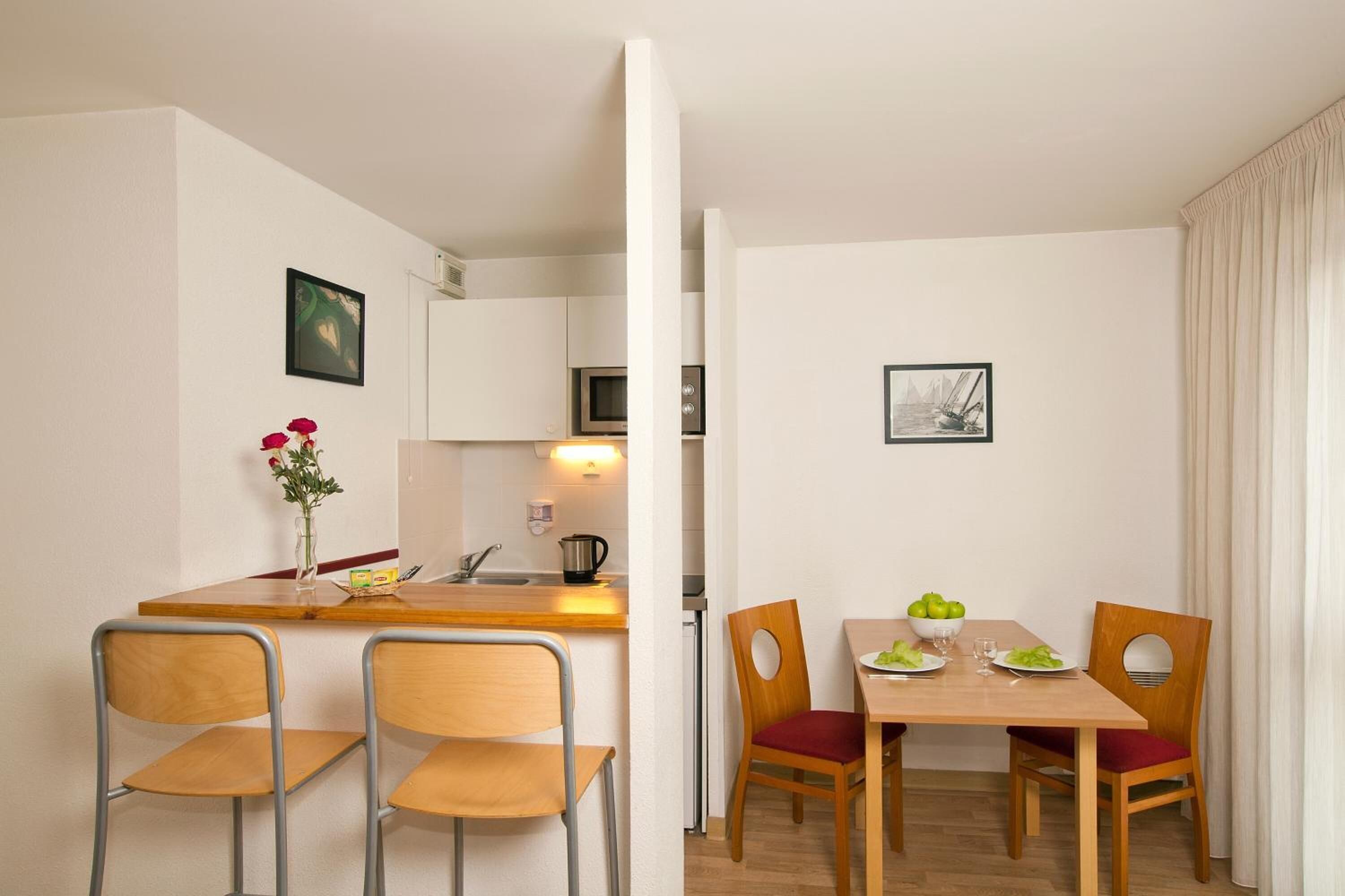 Una cocina compacta con comedor, que incluye una mesa de madera, sillas y un jarrón con flores.