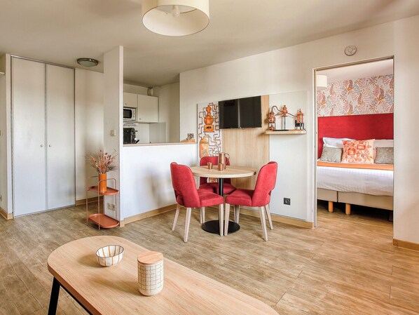 A compact hotel room with a kitchenette, a dining area with red chairs, and a bed with a red headboard. - Séjours & Affaires Angers Atrium (Angers)