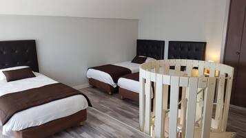 Une chambre d’hôtel avec deux lits, chacun doté d’une tête de lit sombre et de draps blancs. Un berceau blanc est placé dans un coin de la pièce.