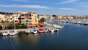 A marina with multiple boats docked, a building with balconies, and a clear sky.