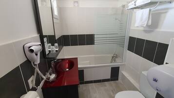 Un baño con un lavamanos rojo, un inodoro blanco, una ducha con mampara de vidrio y un secador de pelo en la pared.