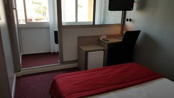 Una habitación de hotel con cama, un escritorio pequeño, televisión y ventana con cortinas.