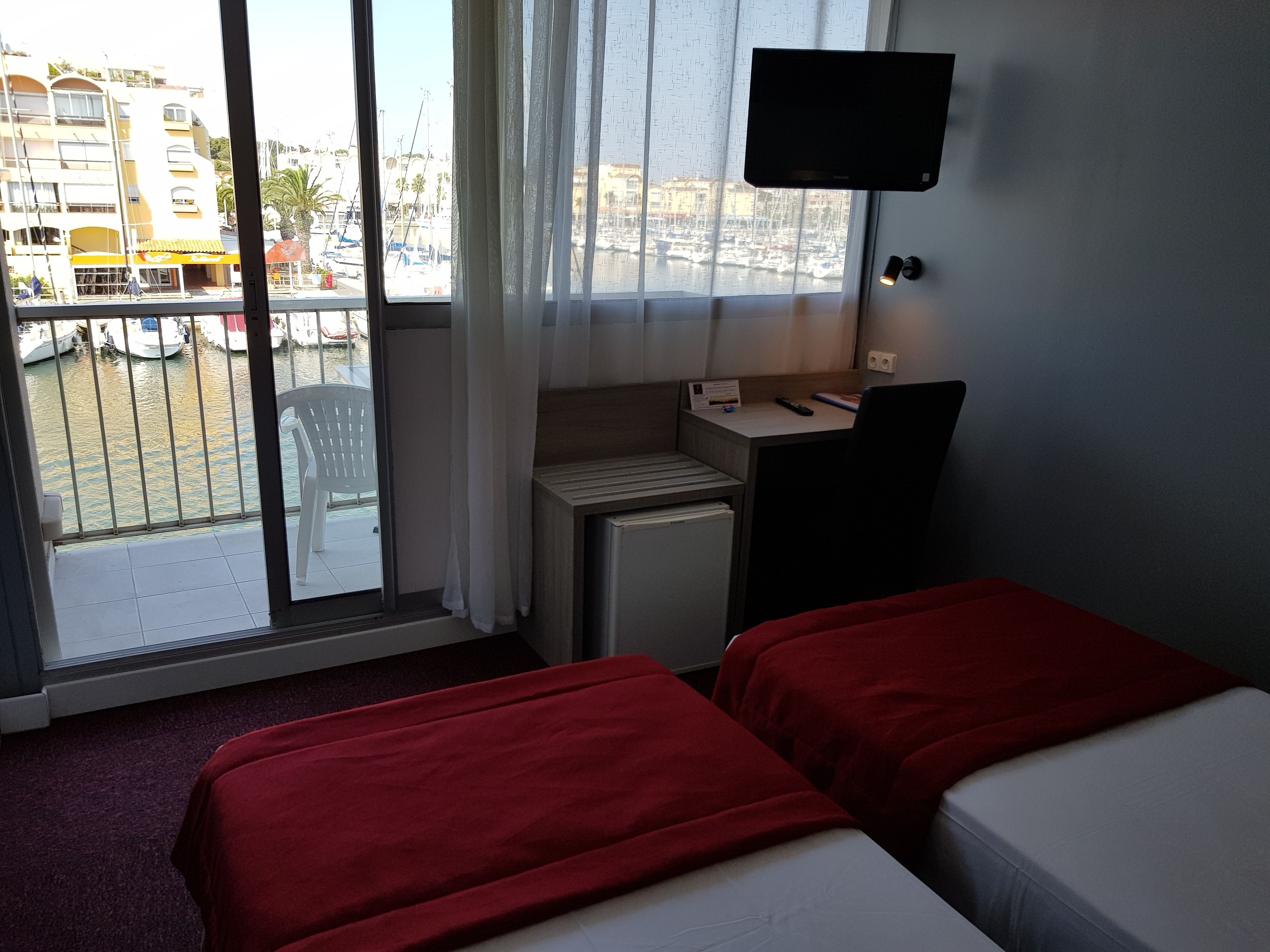 A hotel room with two beds, a desk, a TV, and a view of the marina.