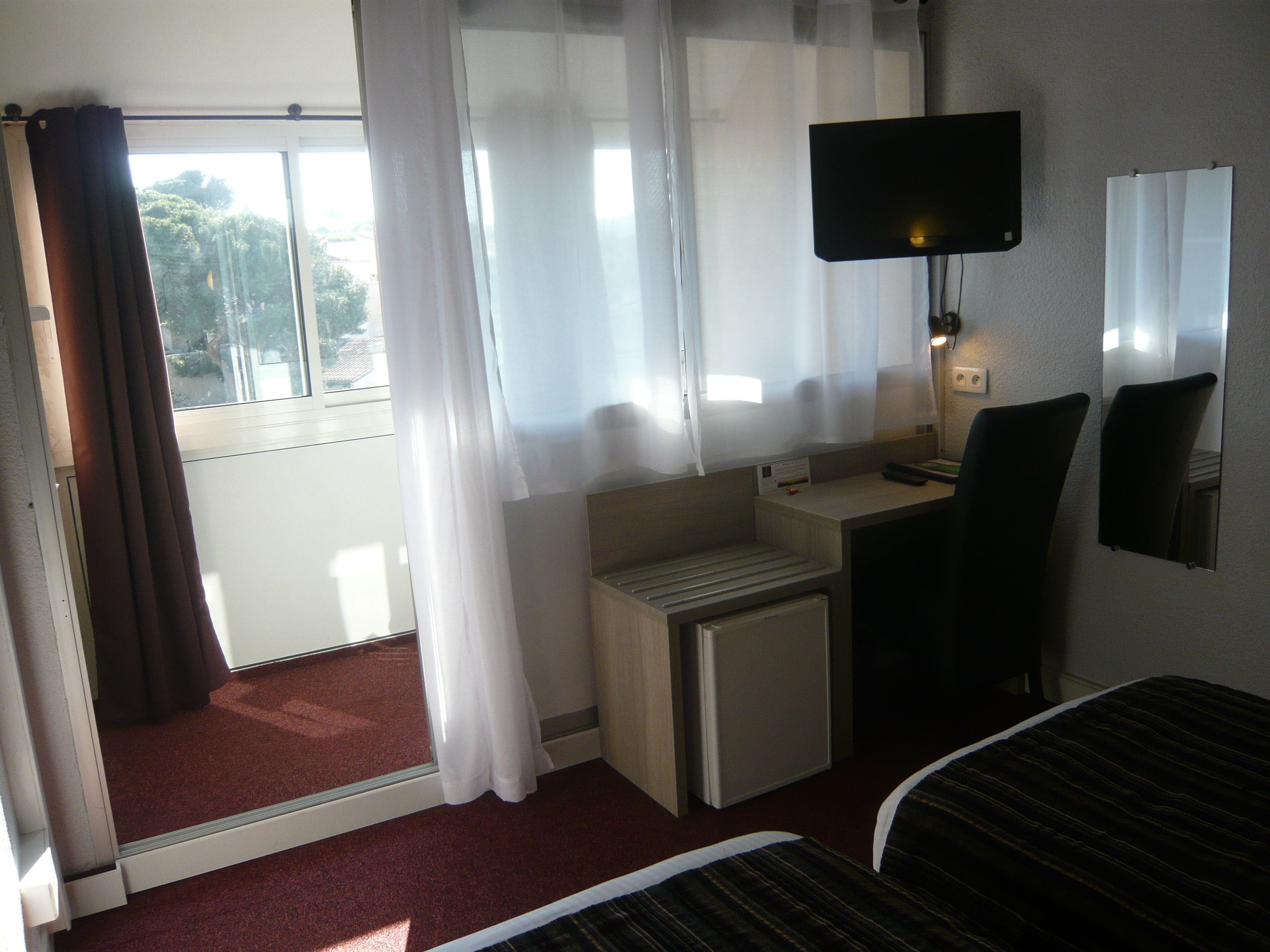A hotel room with a bed, a desk, a chair, a TV, and a window with curtains.