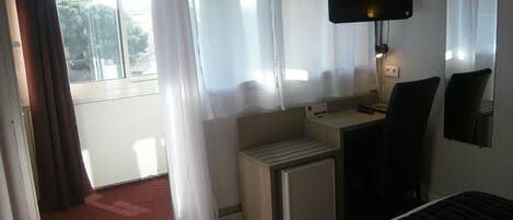 A hotel room with a bed, a desk, a chair, a TV, and a window with curtains.