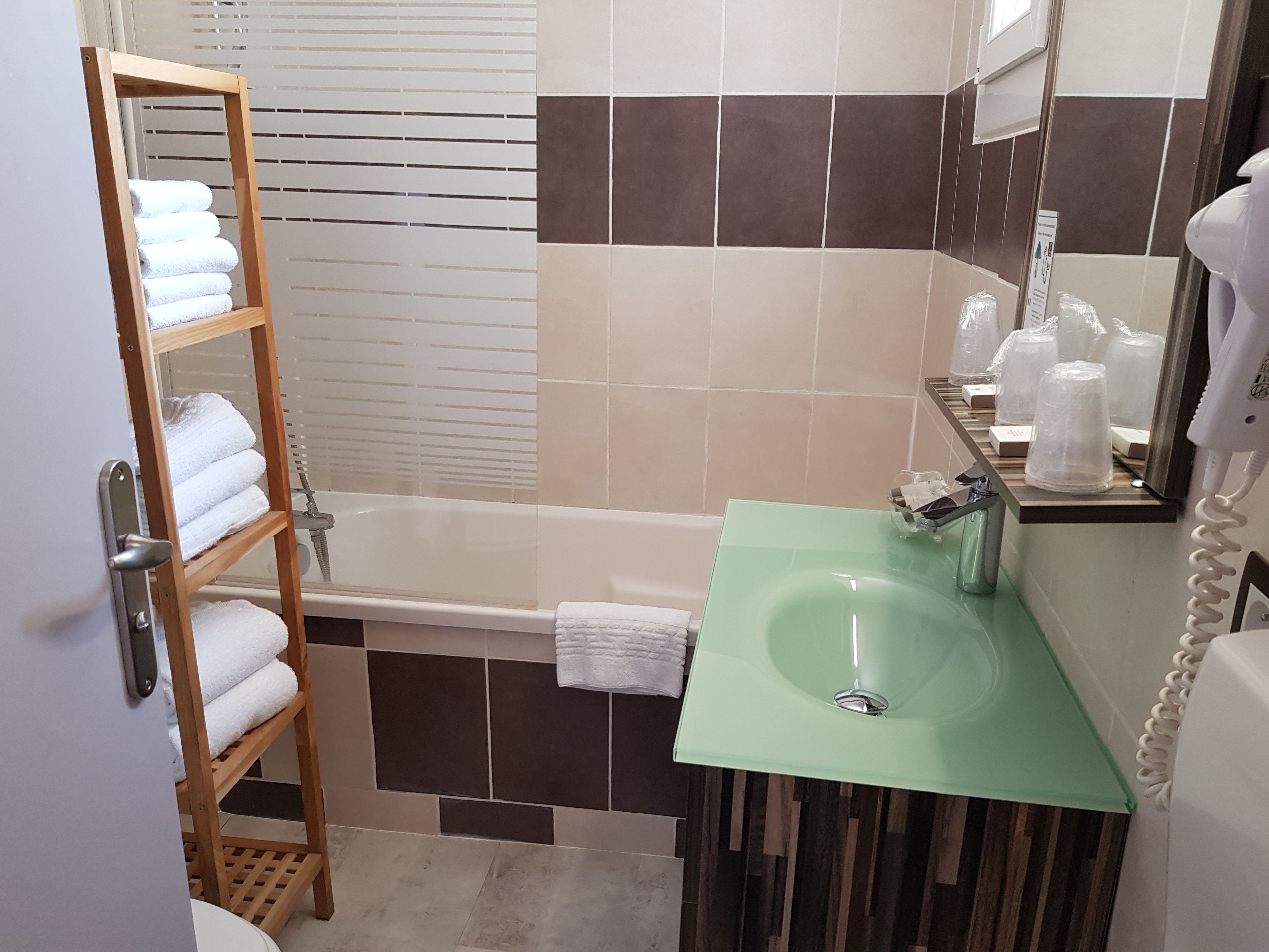 Une salle de bain avec un porte-serviettes en bois, un lavabo vert, une baignoire et un miroir muni d’un téléphone.