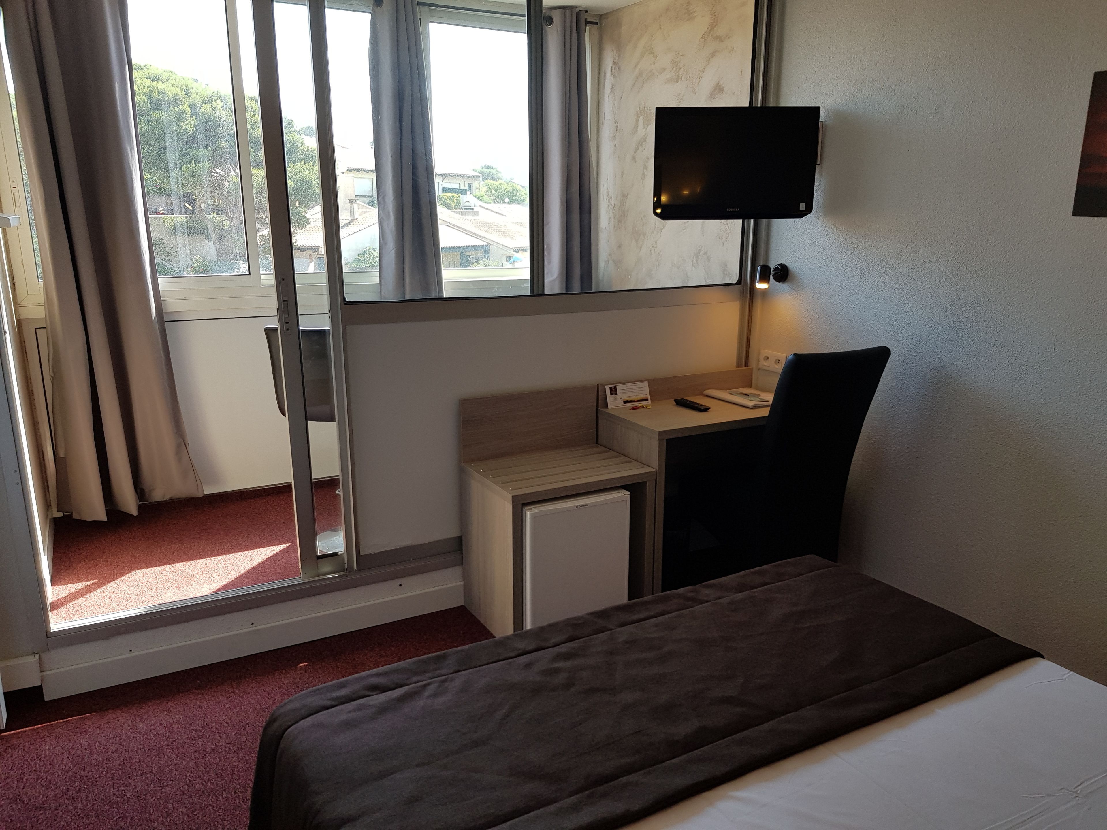 Una habitación de hotel con una cama, un escritorio, un televisor y una ventana con cortinas.