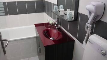 A bathroom with a red sink, a white toilet, and a hairdryer on the wall.