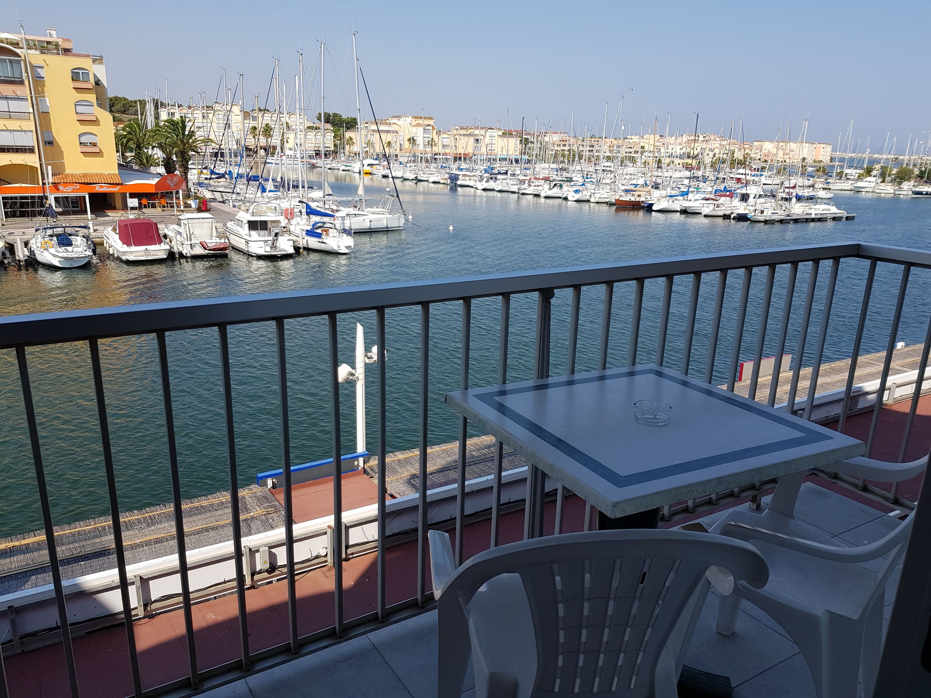 Un balcon avec une table et des chaises donnant sur une marina où sont amarrés de nombreux bateaux.
