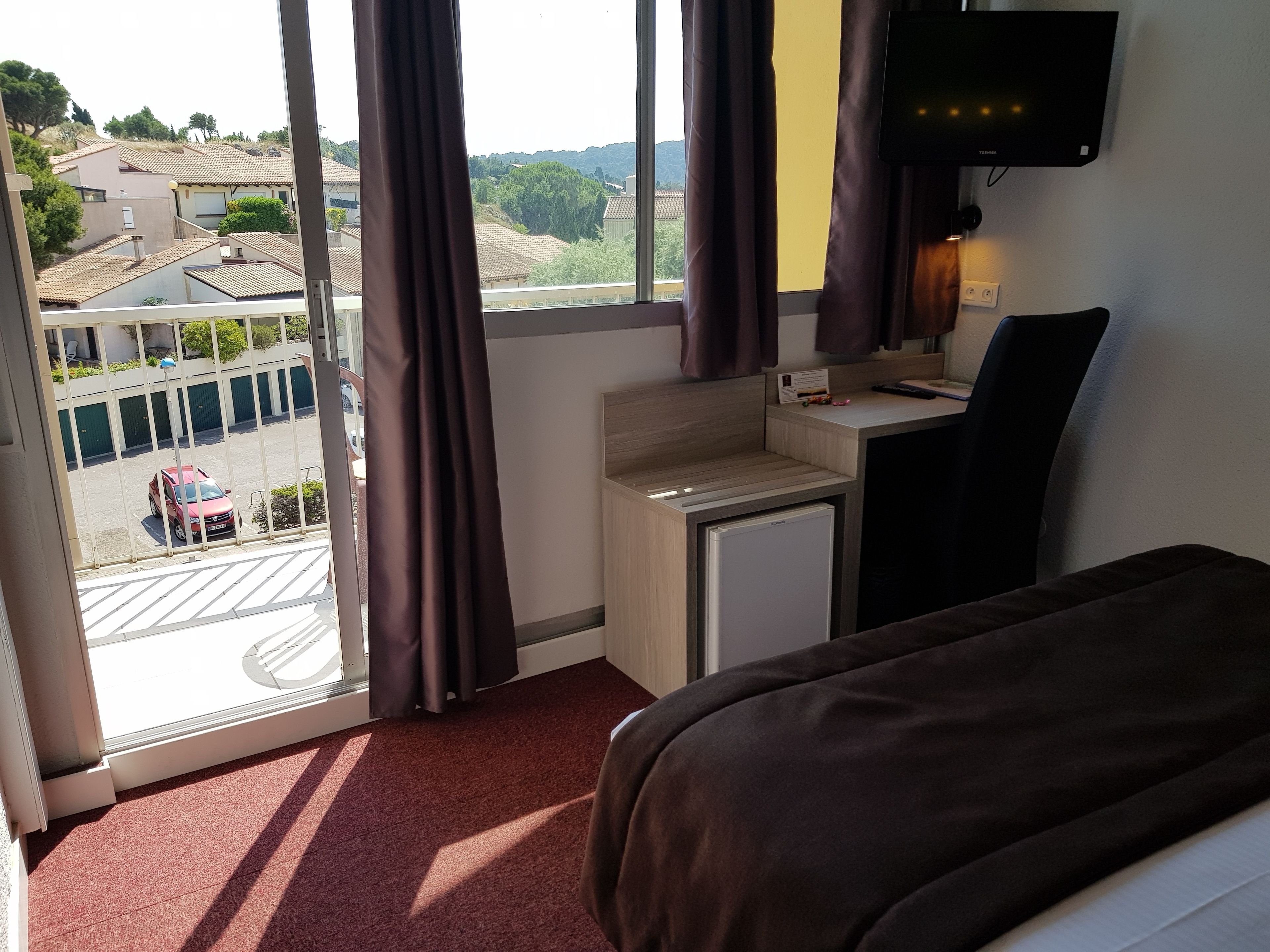 A hotel room with a bed, a desk, a TV, and a view of the outside.