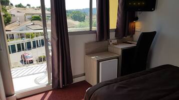 A hotel room with a bed, a desk, a TV, and a view of the outside.