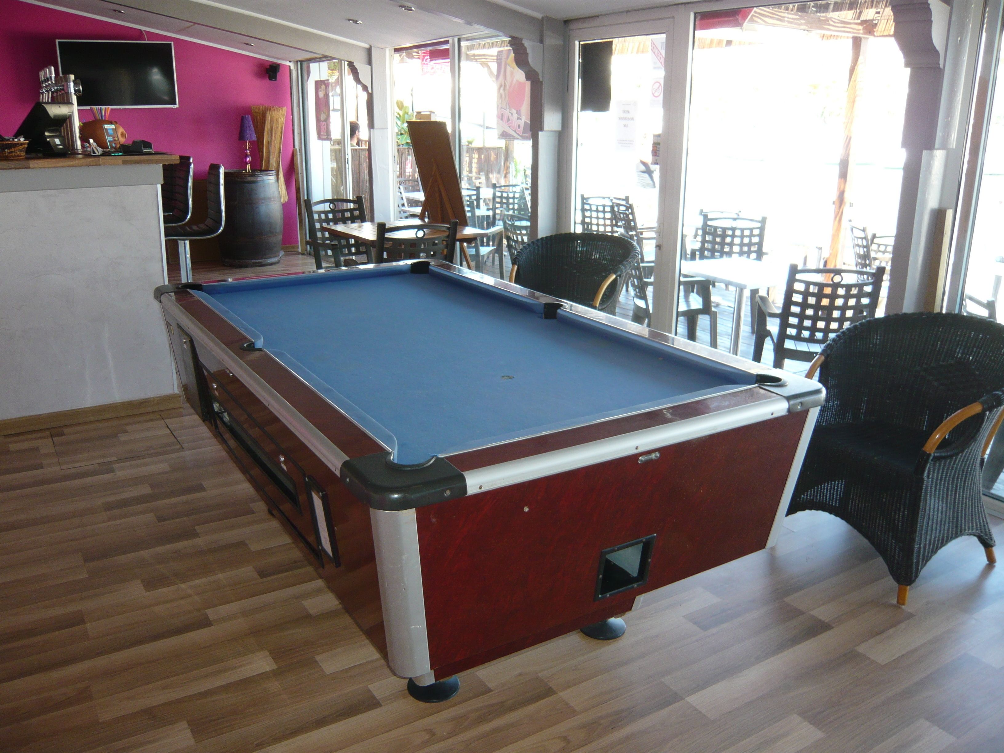 Ein Billardtisch in einem Raum mit Holzboden, einer Bar und einer Sitzgelegenheit mit Stühlen und Tischen.