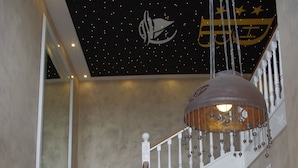 A grand staircase with black carpeted steps and white balusters, leading to a second floor with a starry ceiling and a large hanging light fixture.