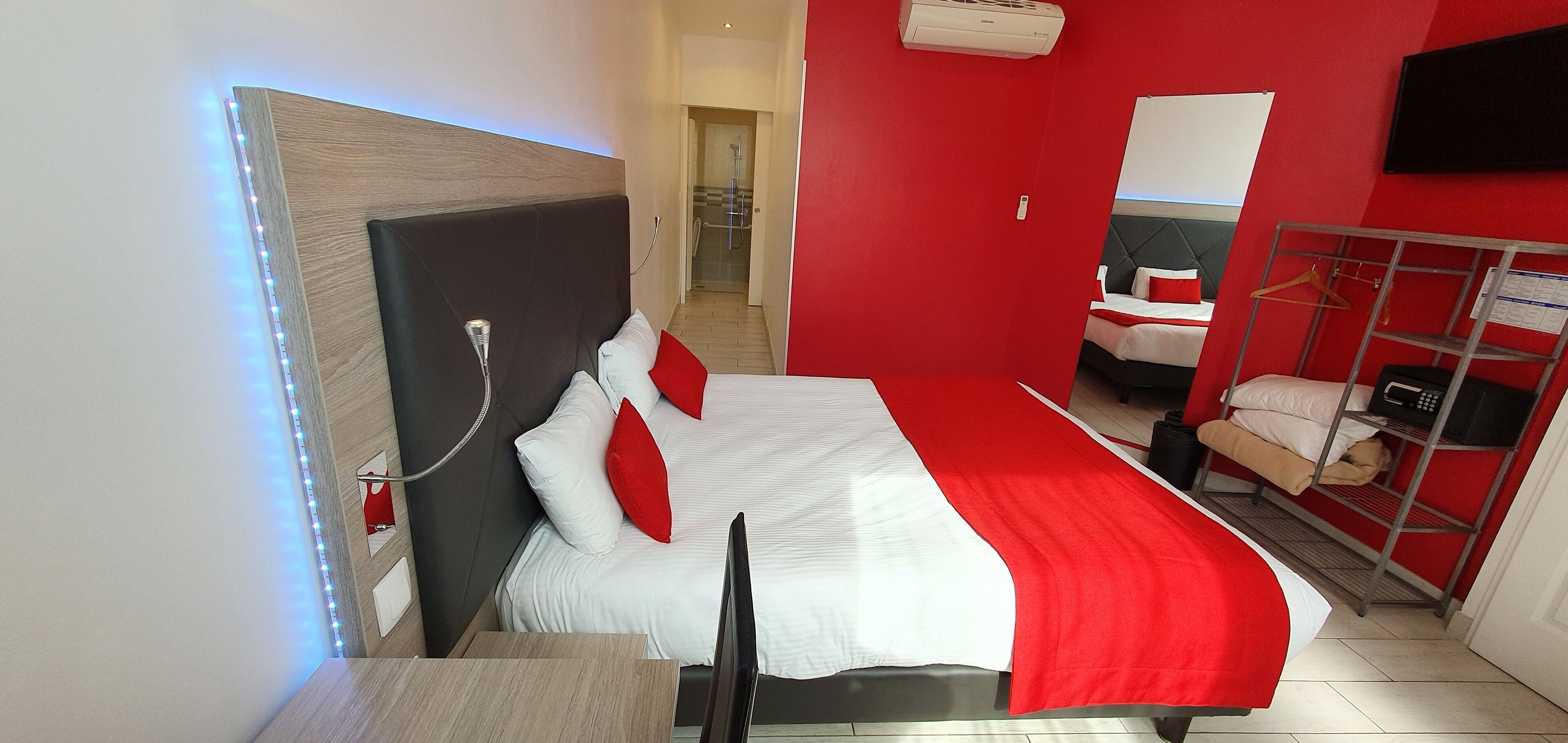 Ein modernes Hotelzimmer mit Bett, Fernseher, einer roten und weißen Farbgestaltung sowie einem Duschbereich.