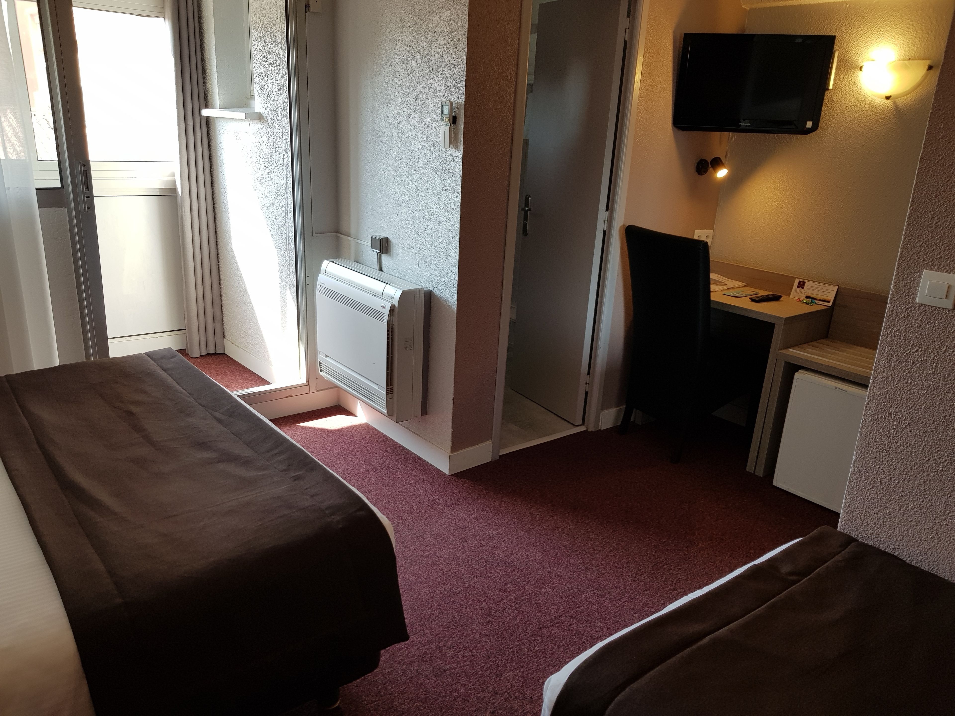 Habitación de hotel con dos camas, un escritorio pequeño, televisión y calefacción.