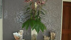 Uma mesa branca com um vaso de flores, uma vela e um pequeno objeto decorativo.