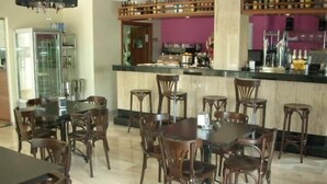 Um restaurante com várias mesas e cadeiras de madeira, um bar com prateleiras cheias de garrafas e uma cozinha ao fundo.