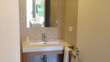 Un baño con pared de azulejos, un lavamanos, un espejo y un perchero para toallas.