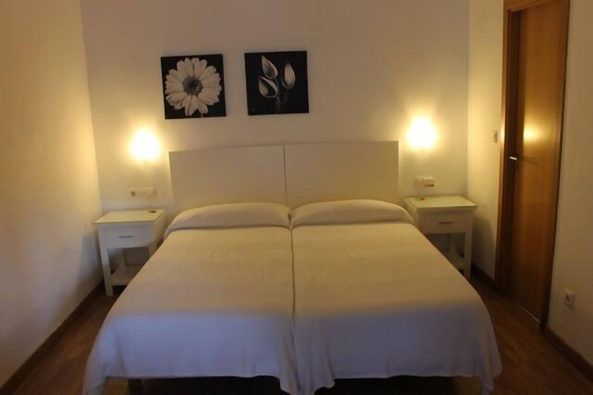 A double bed with white bedding, two bedside tables, and wall-mounted lamps.
