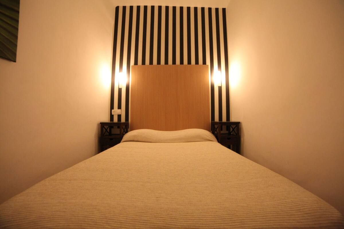 A neatly made bed with a wooden headboard, flanked by two nightstands with wall-mounted lamps.