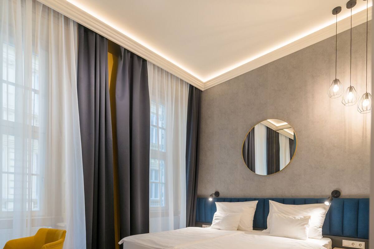 A modern hotel room with a large bed, a bedside table, a chair, and a window with curtains.