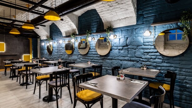 En restaurant med flere borde og stole, stenvægge og gule hængende pendellamper.