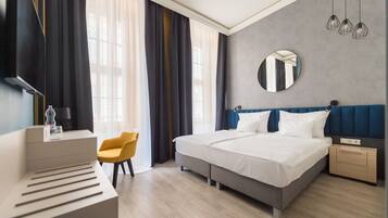 Una habitación de hotel moderna con cama, mesita de noche, silla y un amplio ventanal con cortinas.