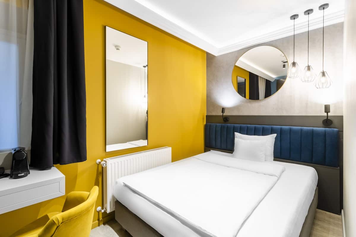 A hotel room with a bed, a mirror, a radiator, and a chair.